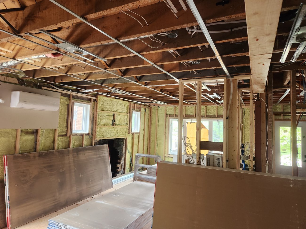 Full-room renovation in progress with strapped ceiling and drywall sheets staged for installation
